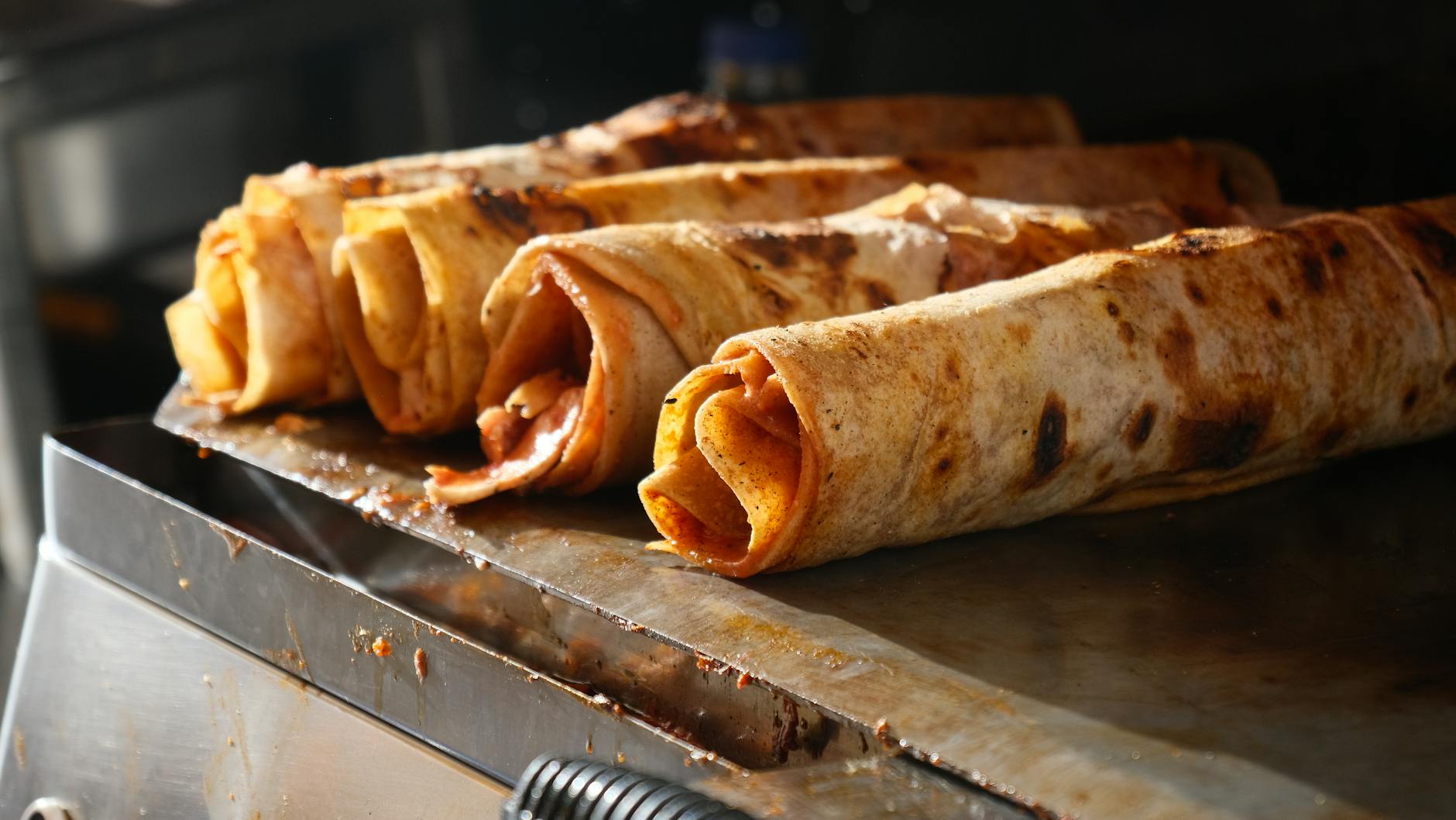 Rolled flatbread wraps browning on a griddle