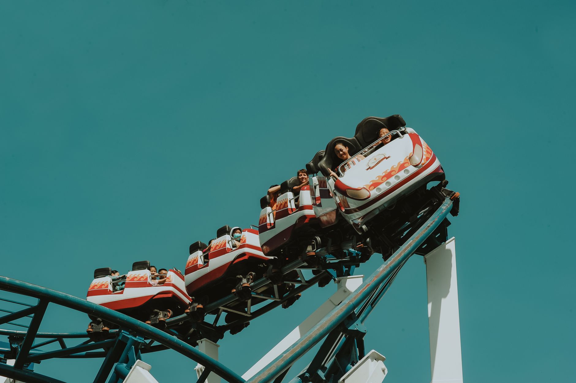Riders on a rollercoaster at a theme park against a blue sky