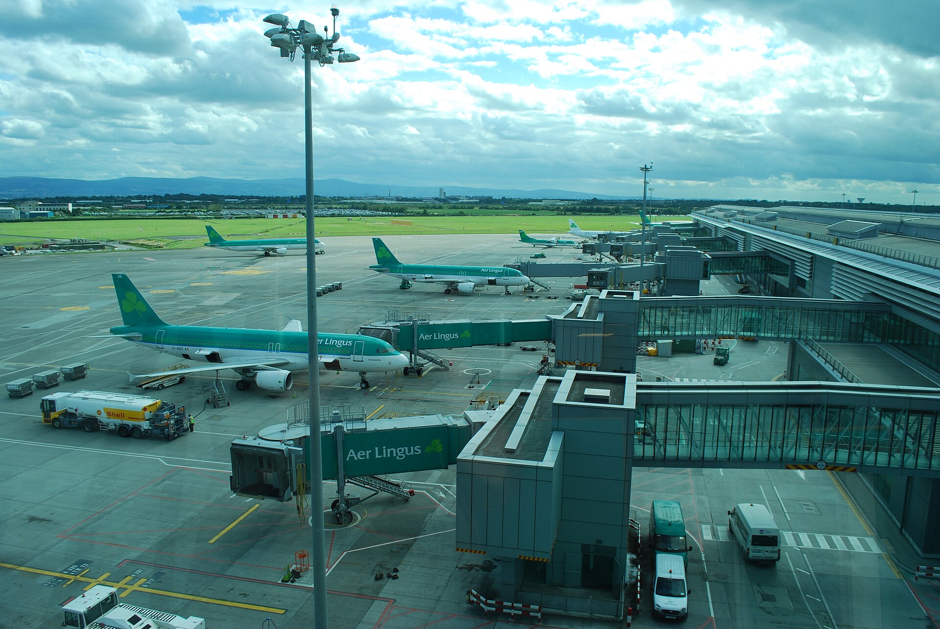 Aer Lingus aircraft stand beside jet bridges at Dublin Airport Terminal 2, with the runway area beyond.