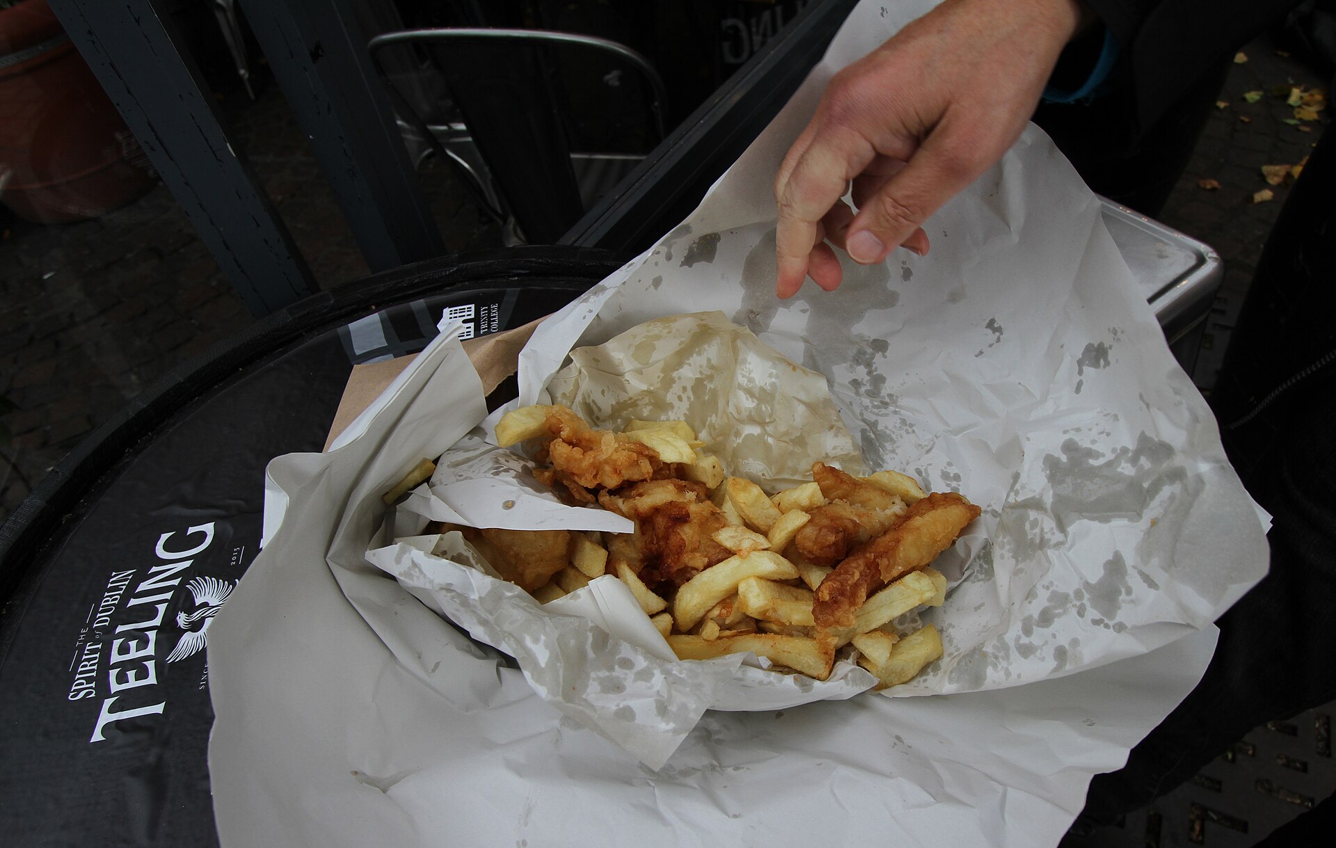 Battered fish and thick chips from Leo Burdock in Dublin, unwrapped on white paper at an outdoor table.