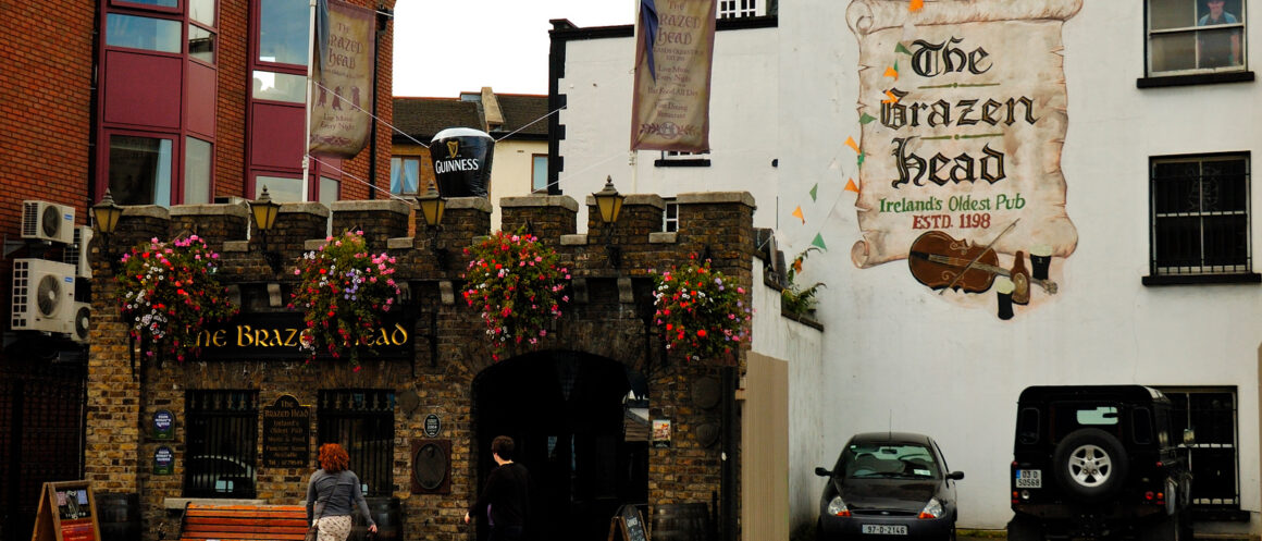 The Brazen Head in Dublin, with a stone entrance arch, hanging flowers and a painted sign on its white wall.