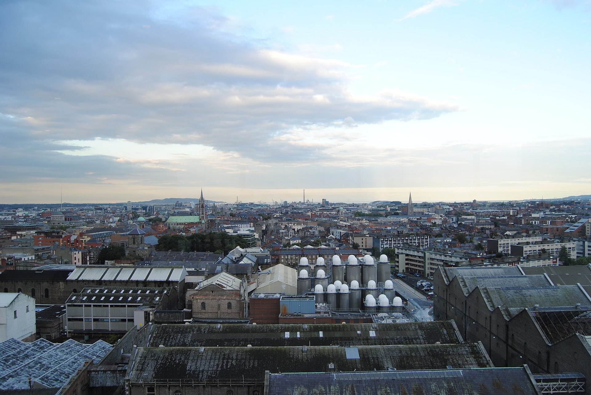 Brewery rooftops and white tanks fill the foreground of the Dublin skyline seen from the Guinness Storehouse.