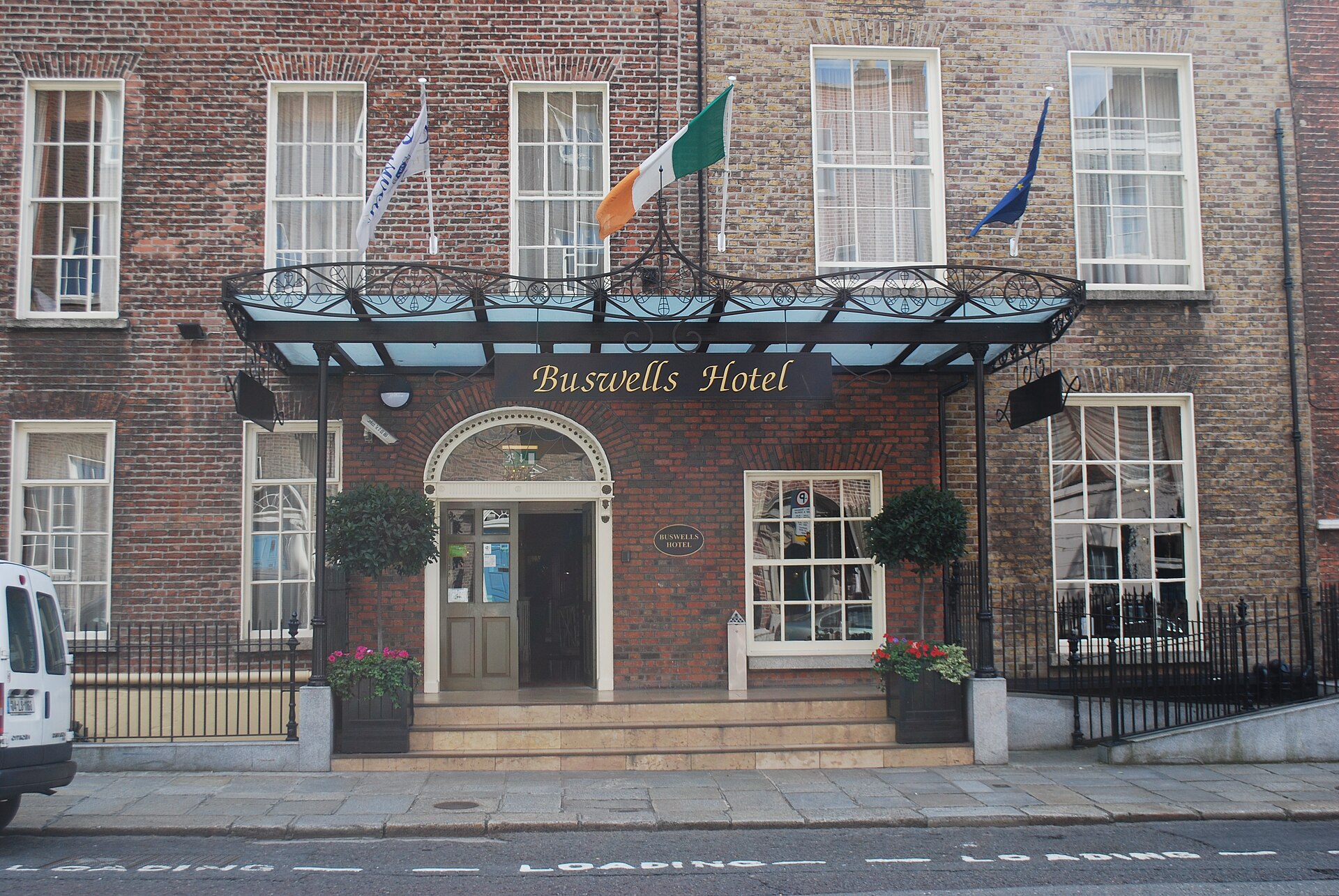 Buswells Hotel in Dublin has a glass canopy, three flags and a brick entrance reached by shallow steps.