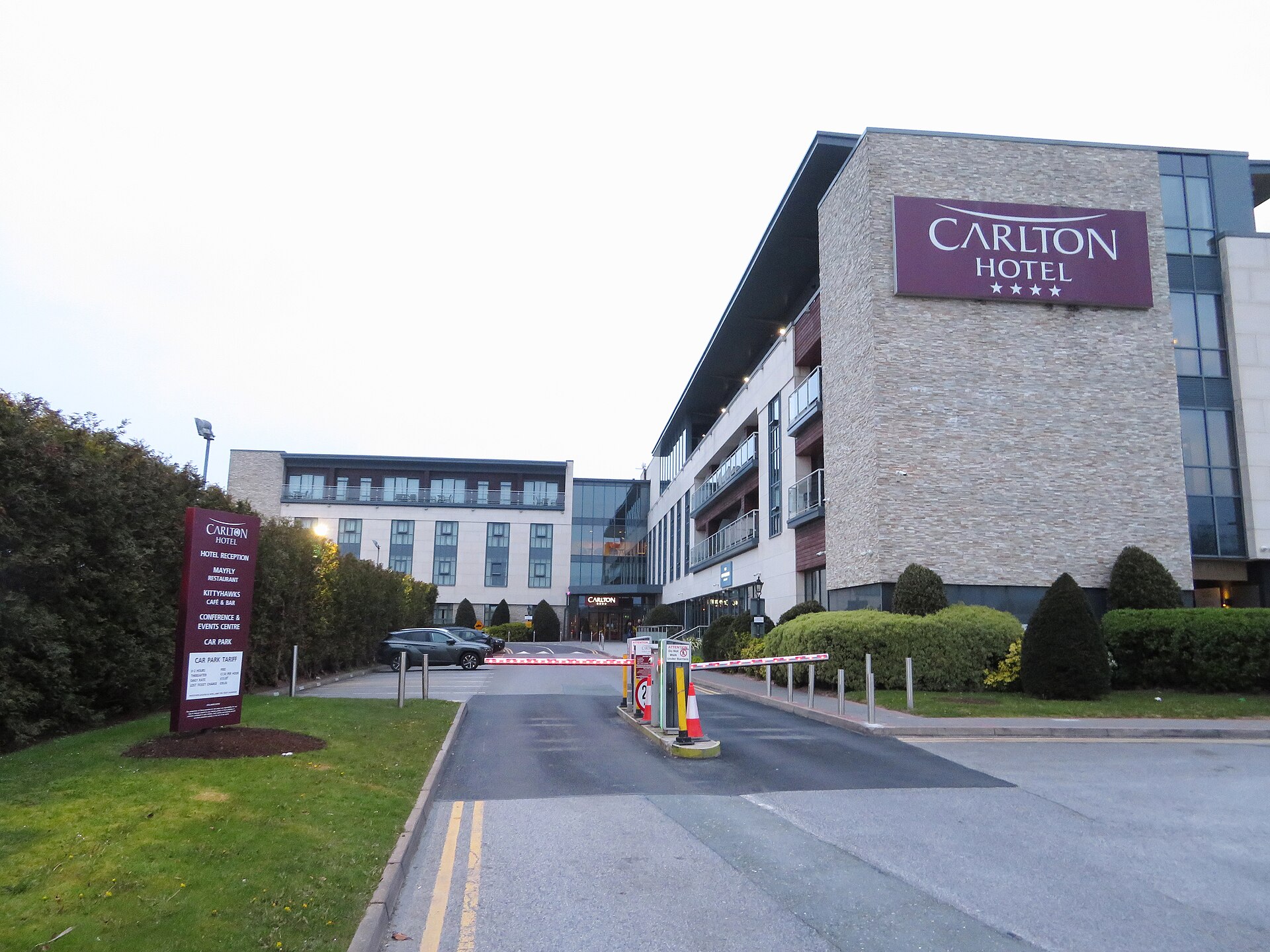 Carlton Hotel Dublin Airport's entrance driveway, with parking barriers and clipped hedges beneath the sign on its stone-clad facade.