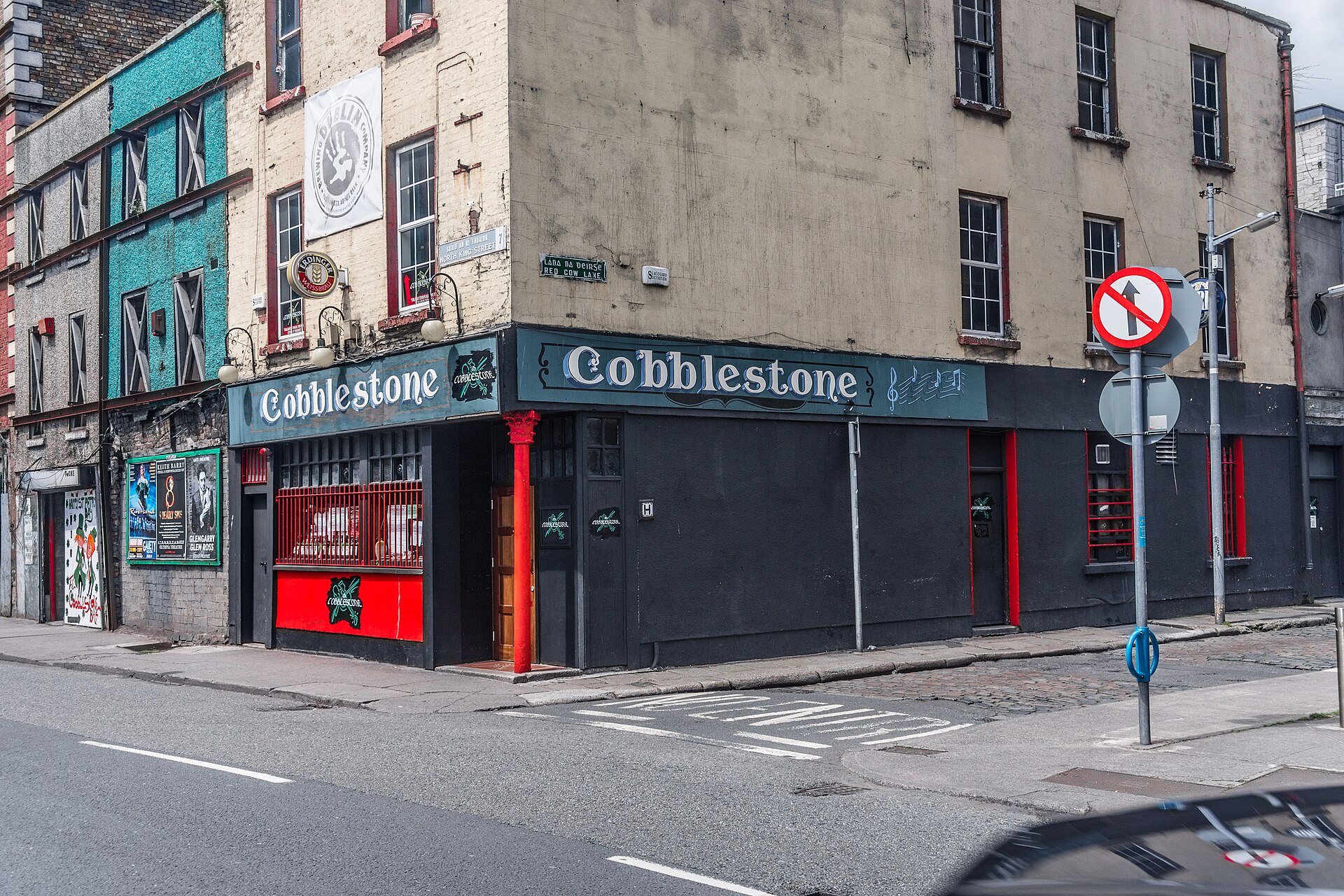 The Cobblestone pub in Dublin seen across a street corner, with red trim and musical notes on its sign.