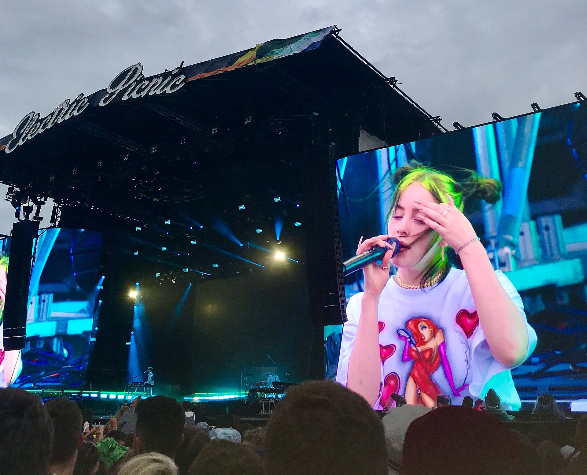 A crowd watches Billie Eilish perform at Electric Picnic, with the singer shown on a large screen beside the stage.