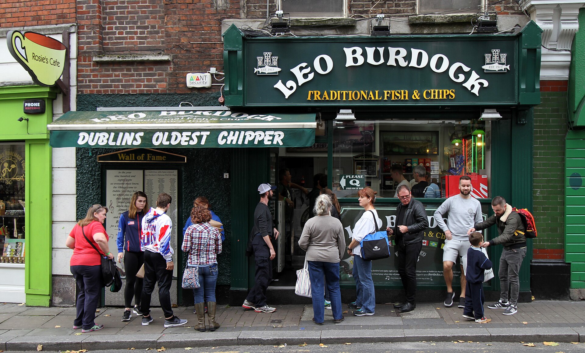 Customers outside Leo Burdock's green Werburgh Street shopfront in Dublin, beneath a large traditional fish-and-chips sign.