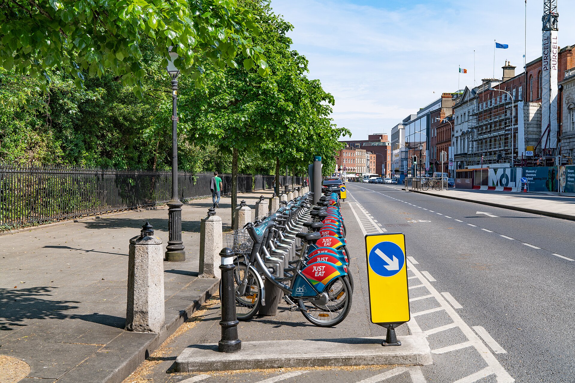 DublinBikes bicycles lined up beside the railings and leafy trees of St Stephen's Green on a sunny Dublin street.
