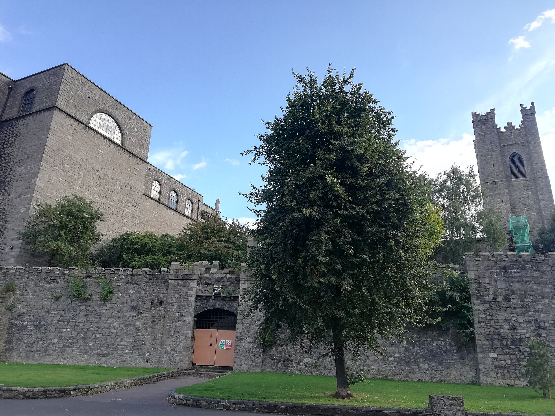 Dublin's medieval city wall and arched St Audoen's Gate stand below church buildings and trees on Cook Street.