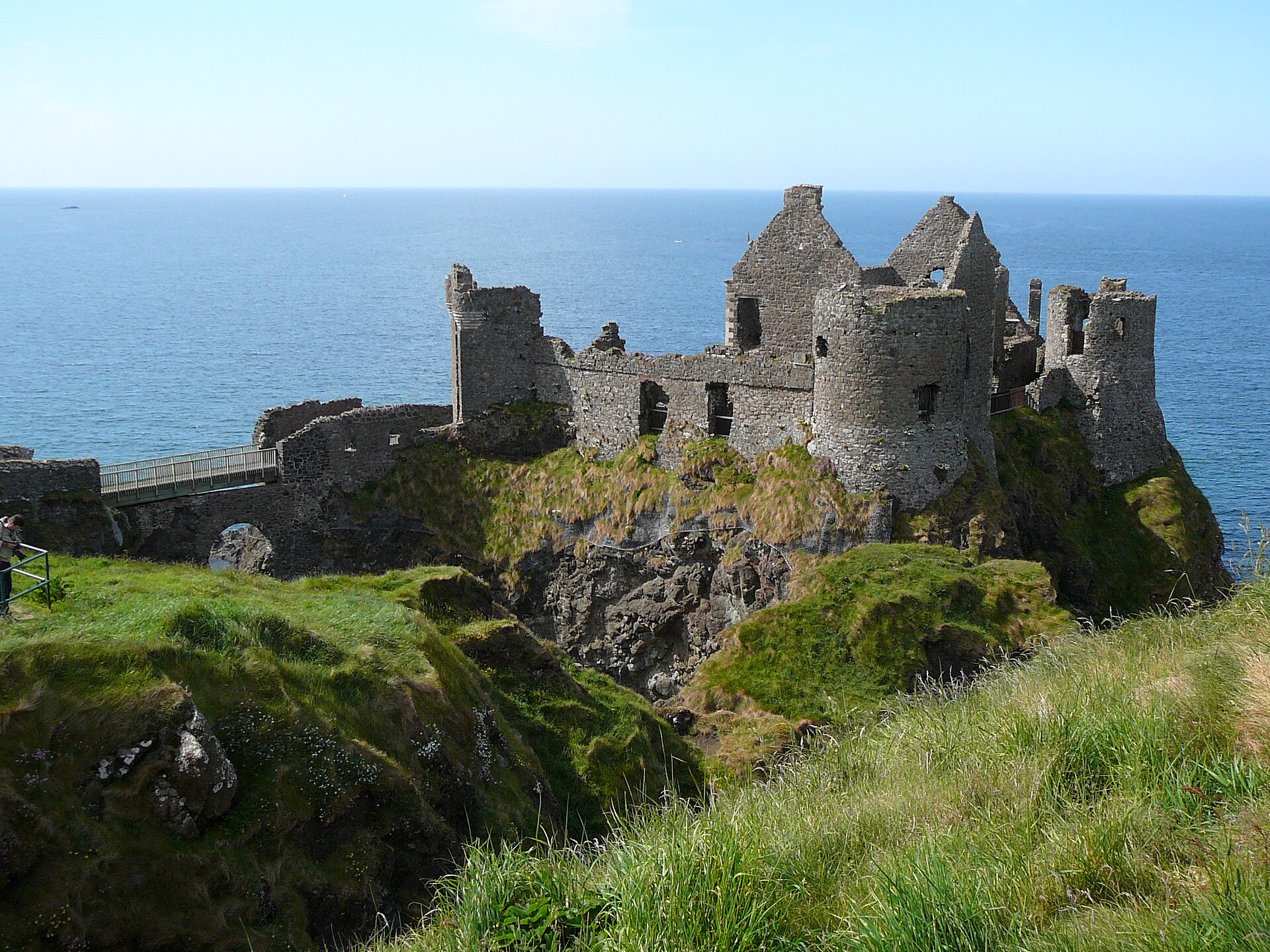 Dunluce Castle's ruined towers stand on a rocky coastal outcrop, with a footbridge crossing the cleft below.