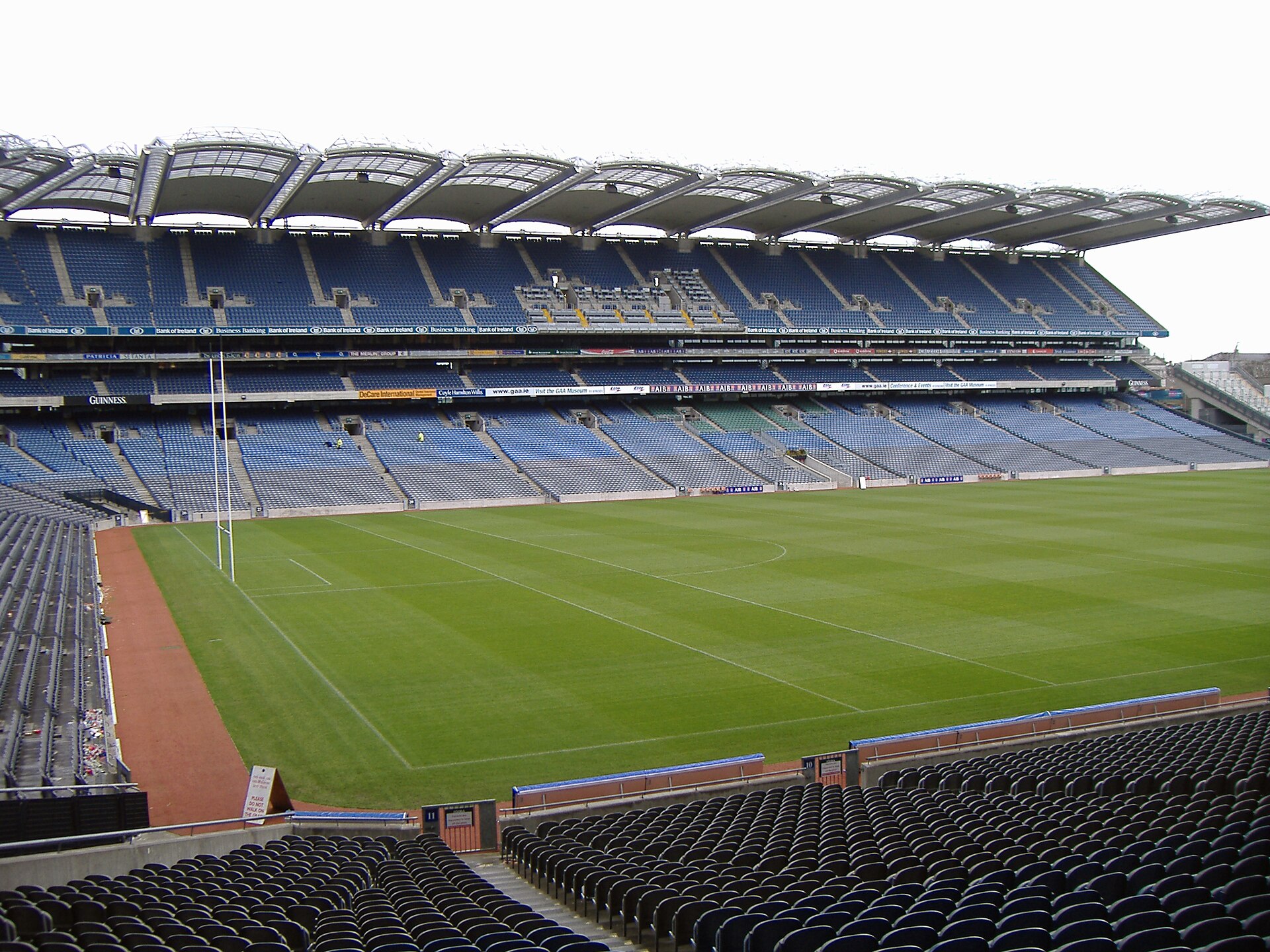 Empty blue seating tiers overlook the green pitch and tall goalposts inside Croke Park stadium in Dublin.