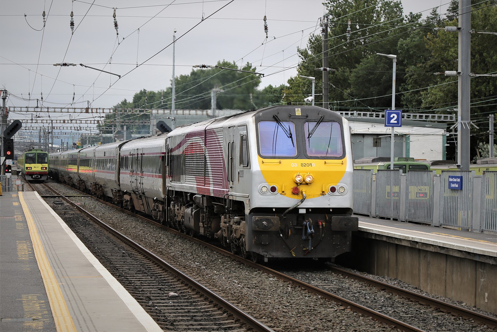 An Enterprise locomotive pulls silver passenger coaches past the platforms at Clontarf Road station in Dublin.