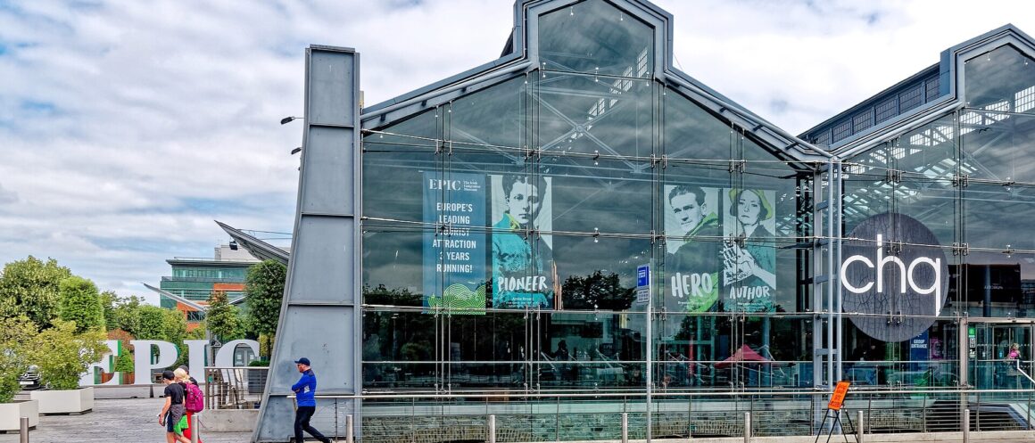 The glass facade of the CHQ Building in Dublin, with EPIC lettering and pedestrians walking along the pavement.