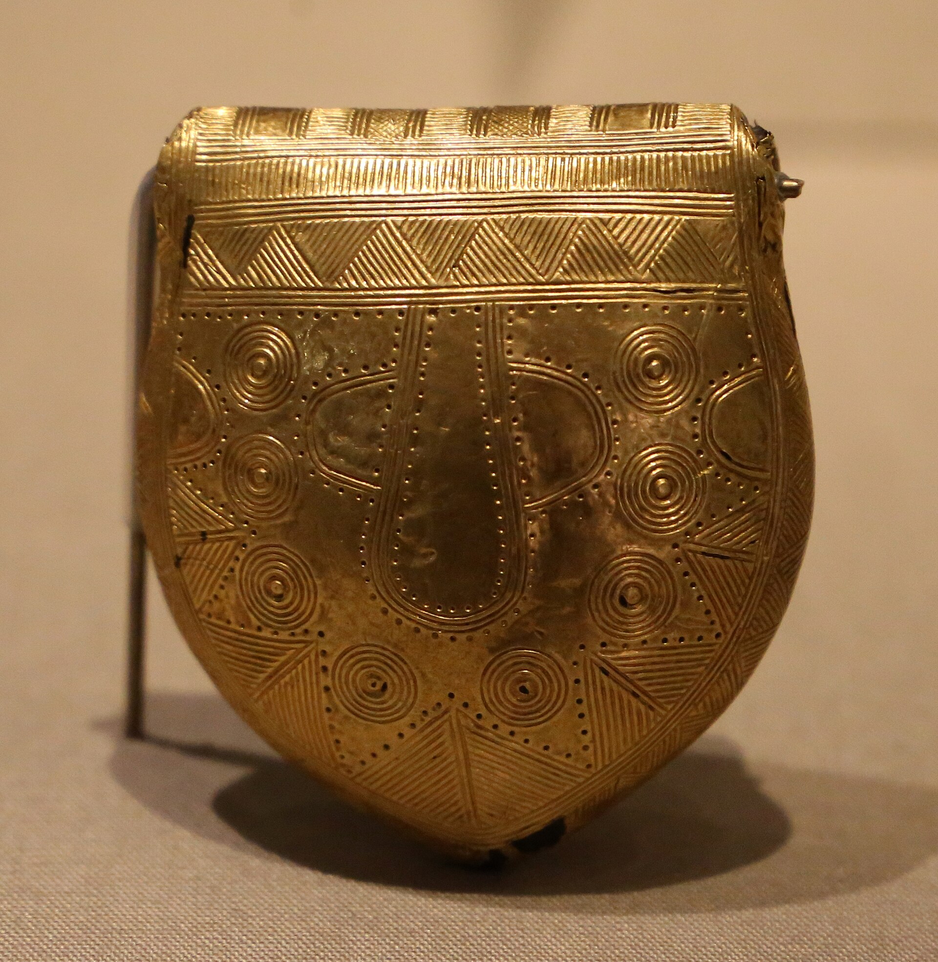 A gold-covered pendant with engraved spirals and triangular patterns stands in the National Museum of Ireland, Dublin.
