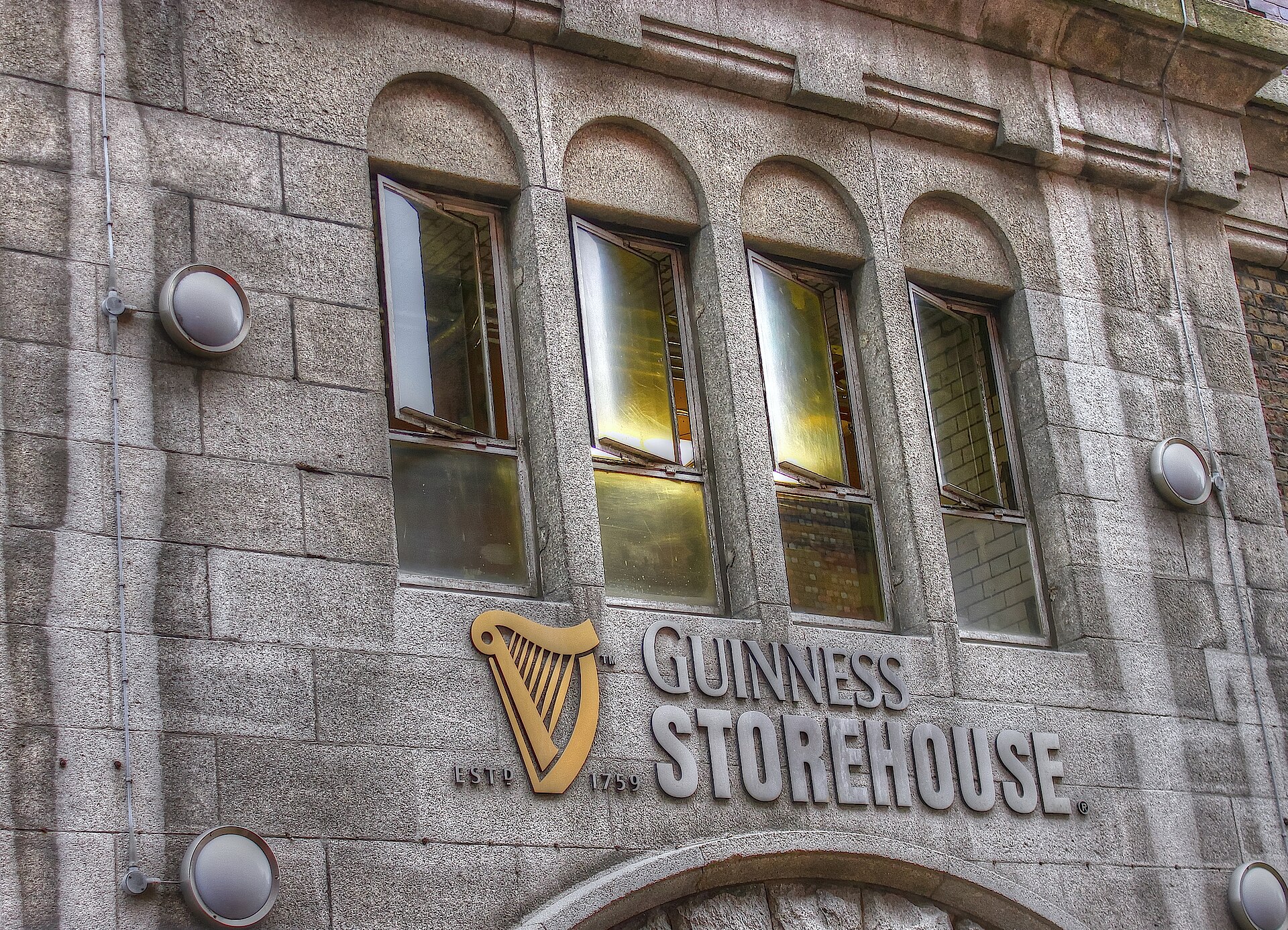 A gold harp and Guinness Storehouse lettering mark the stone facade below tall windows at the Dublin attraction.