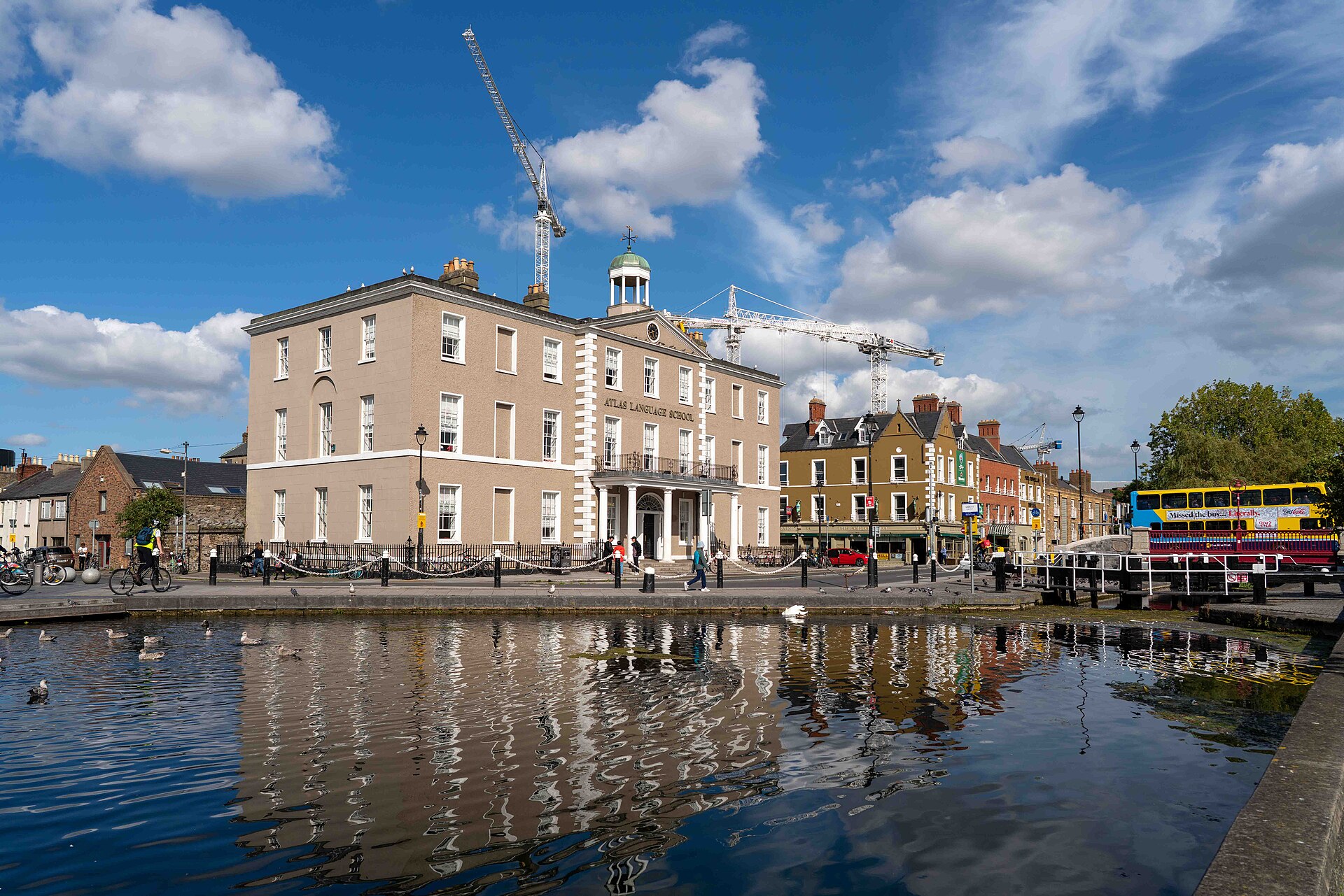 The Grand Canal reflects a pale corner building at Portobello, Dublin, with ducks and pedestrians along the waterside.