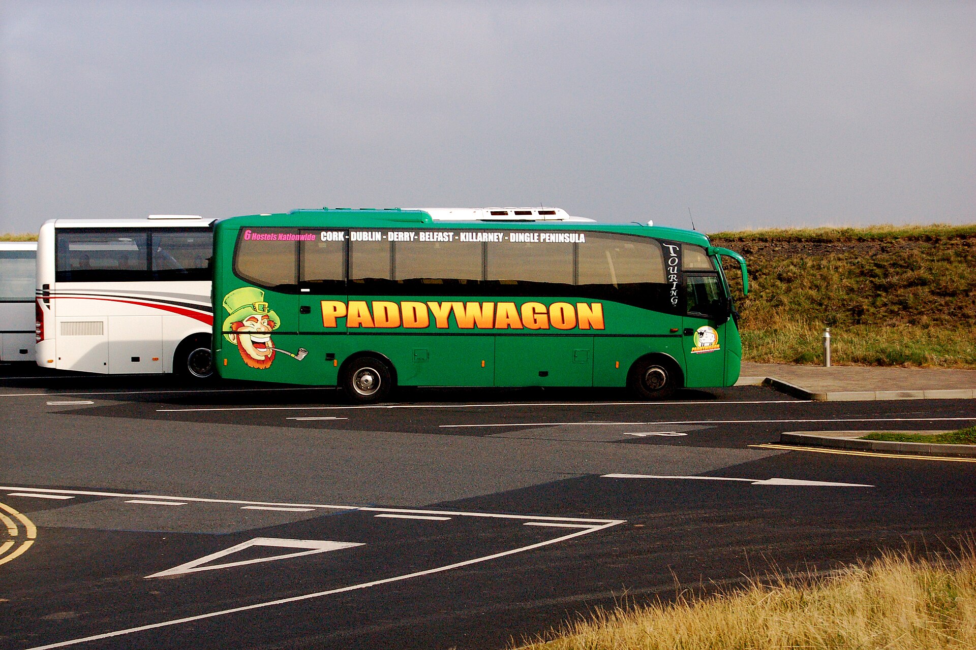 A green Paddywagon tour coach parked beside another coach in the Cliffs of Moher parking area under an overcast sky.