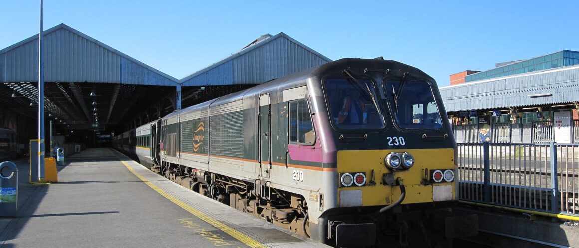 Green and silver Enterprise locomotive and coaches beside the platform at Dublin Connolly station on a sunny day.