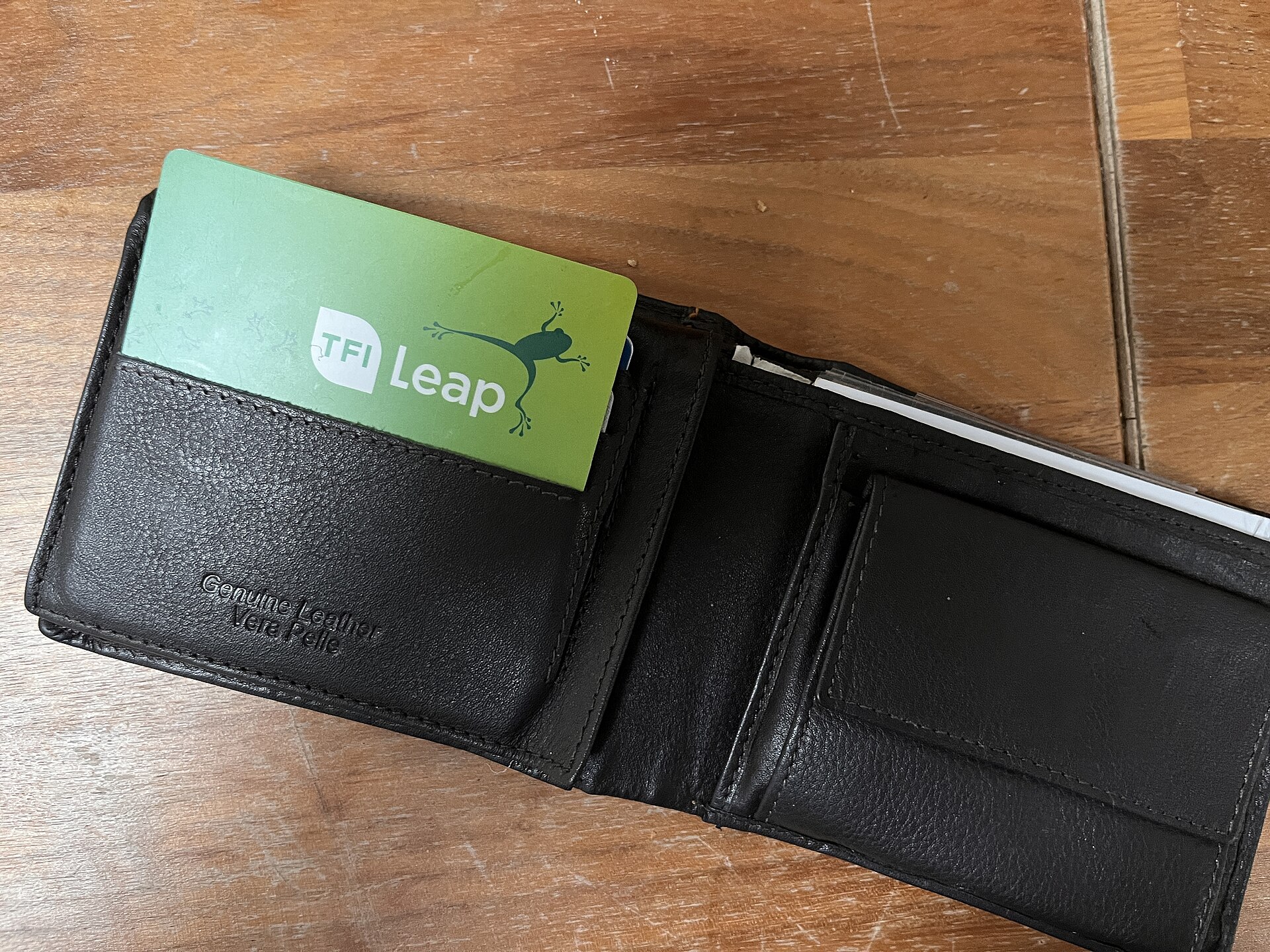 A green TFI Leap card protrudes from an open black leather wallet resting on a wooden table.