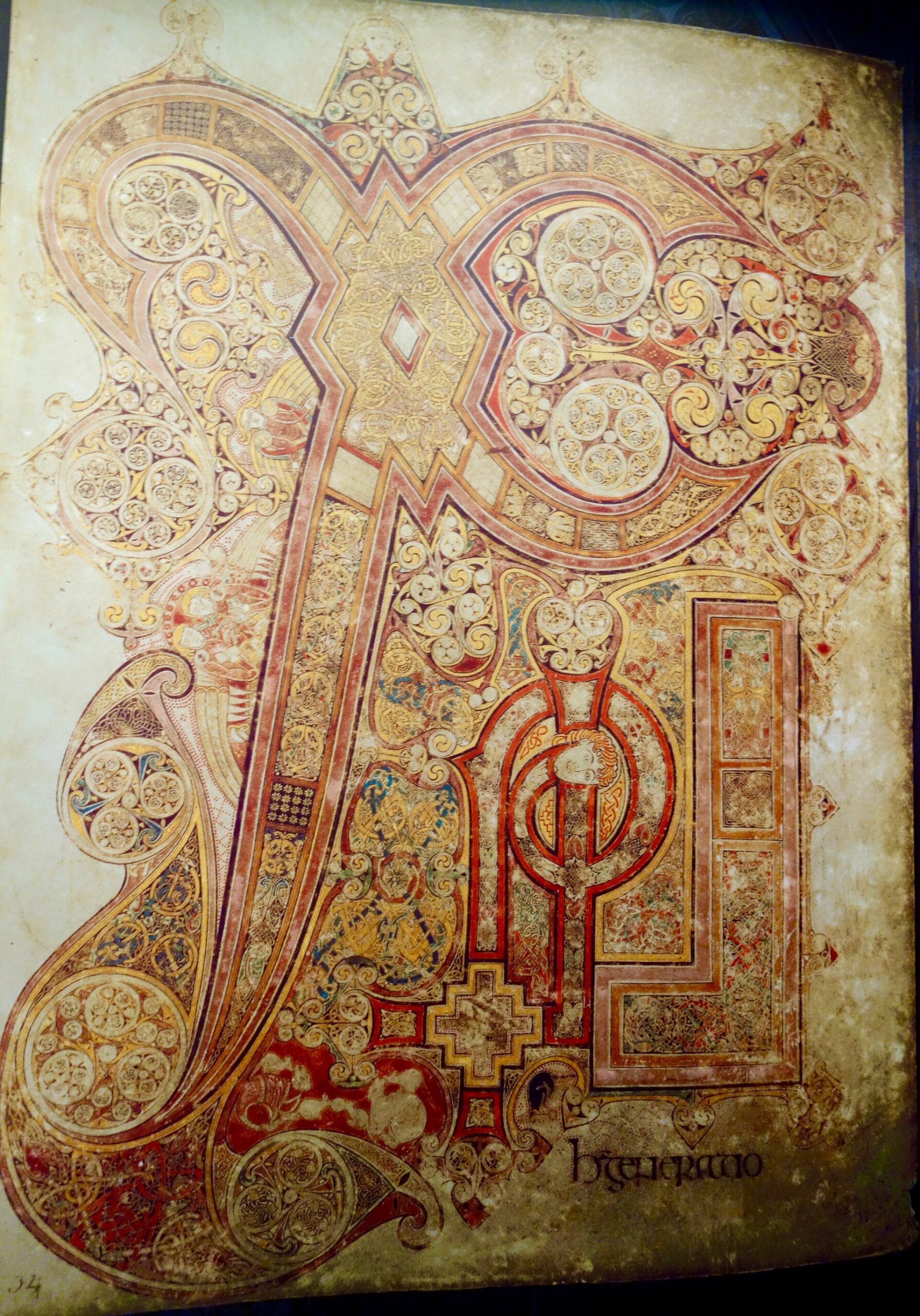 An illuminated Book of Kells page at Trinity College Dublin combines sweeping decorated initials, dense interlace and small painted figures.