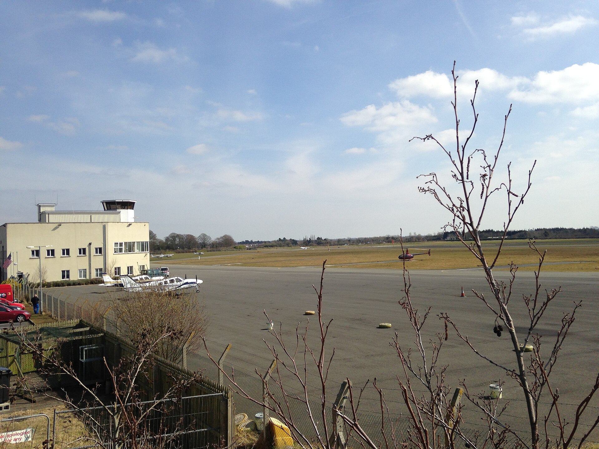Light aircraft and a small helicopter stand beside the apron and grass airfield at Weston Airport near Leixlip, Ireland.