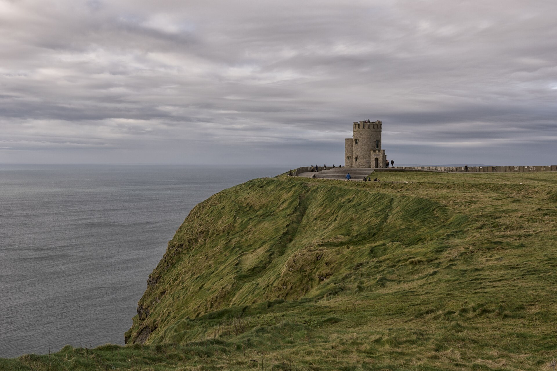 O'Brien's Tower stands on a grassy headland at the Cliffs of Moher above the Atlantic beneath grey clouds.