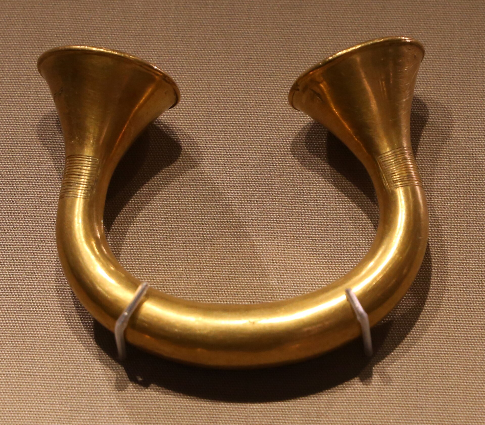 An open gold bracelet with flared ends rests on fabric in the National Museum of Ireland, Dublin.