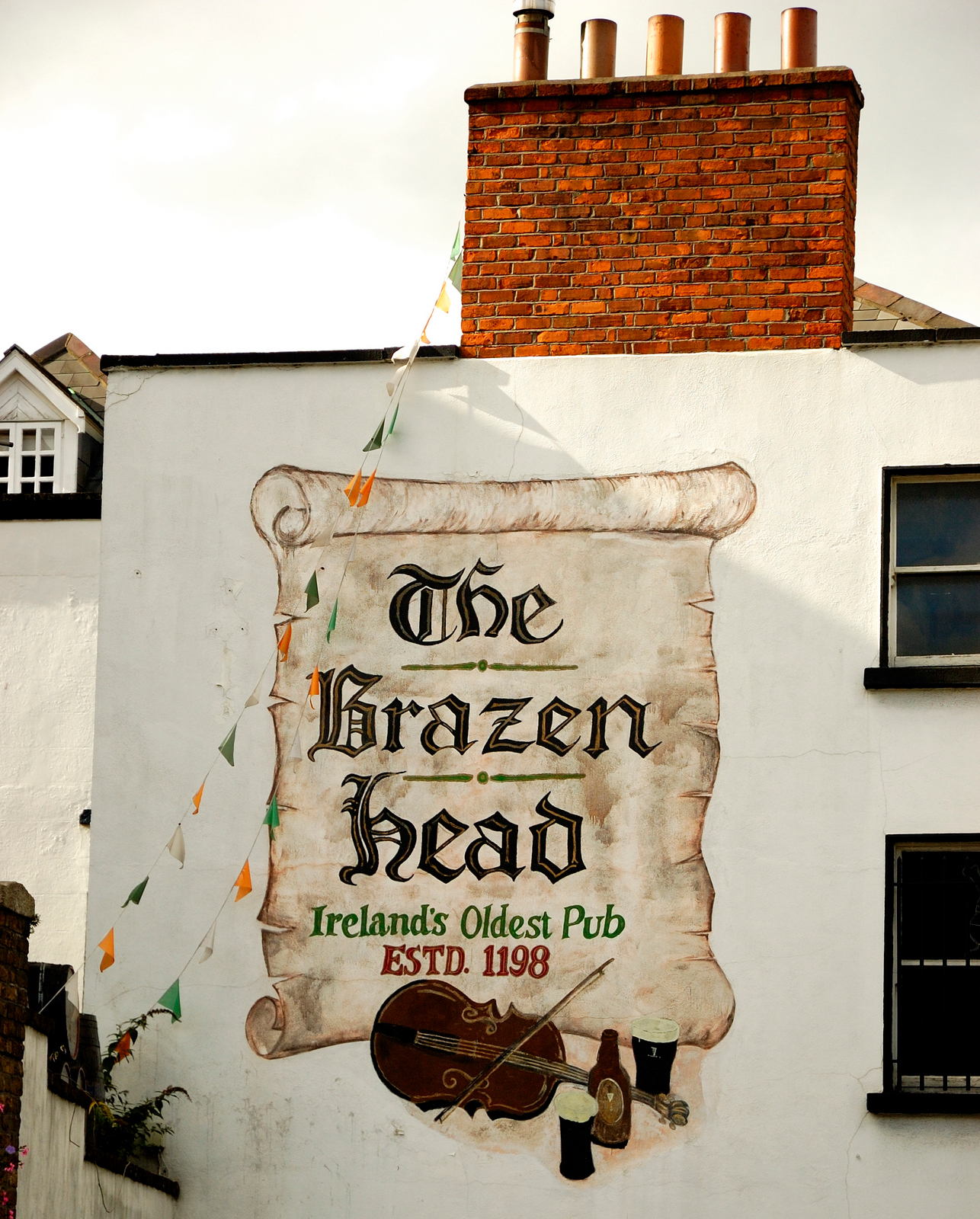 A painted scroll on the Brazen Head in Dublin names the pub beneath a brick chimney and Irish bunting.