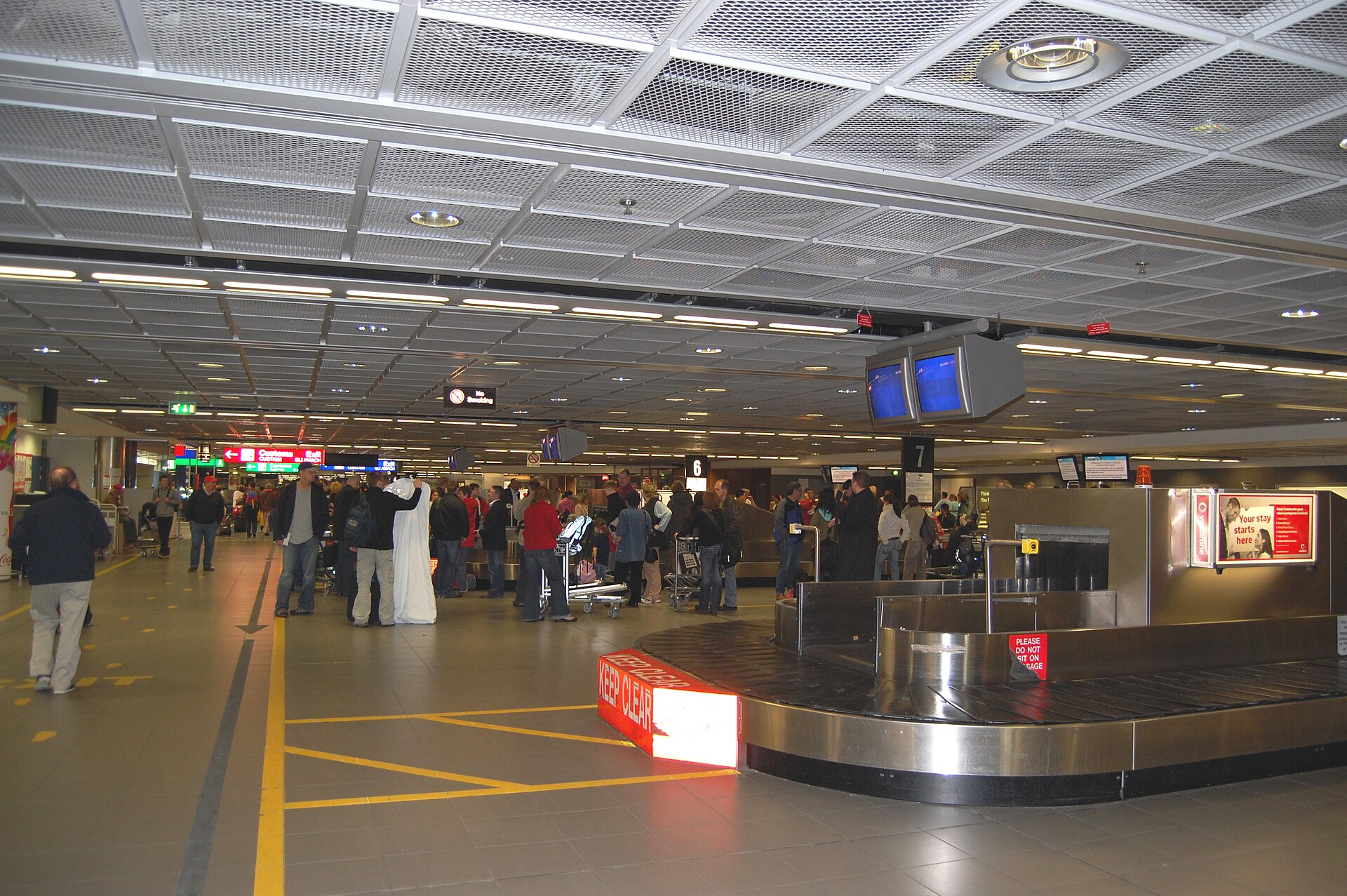 Passengers with luggage trolleys wait beside a baggage carousel in the Dublin Airport arrivals hall.