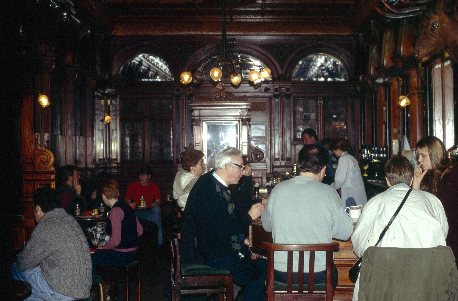 Patrons gather inside Dublin's Stag's Head in 1993, surrounded by carved wood, mirrors, arched glazing and warm globe lamps.
