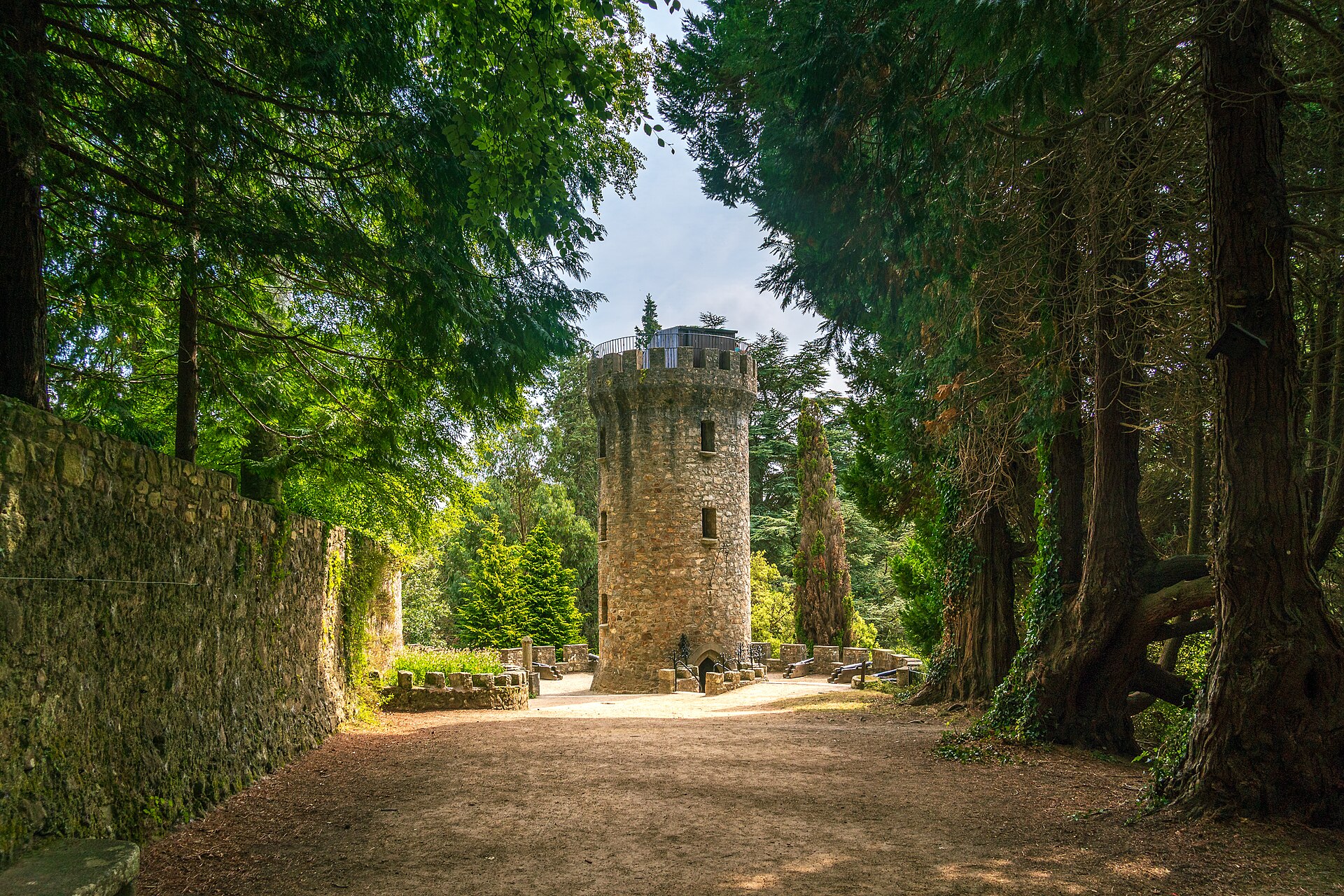 Pepperpot Tower stands at the end of a shaded woodland path in Powerscourt Gardens, surrounded by tall trees.