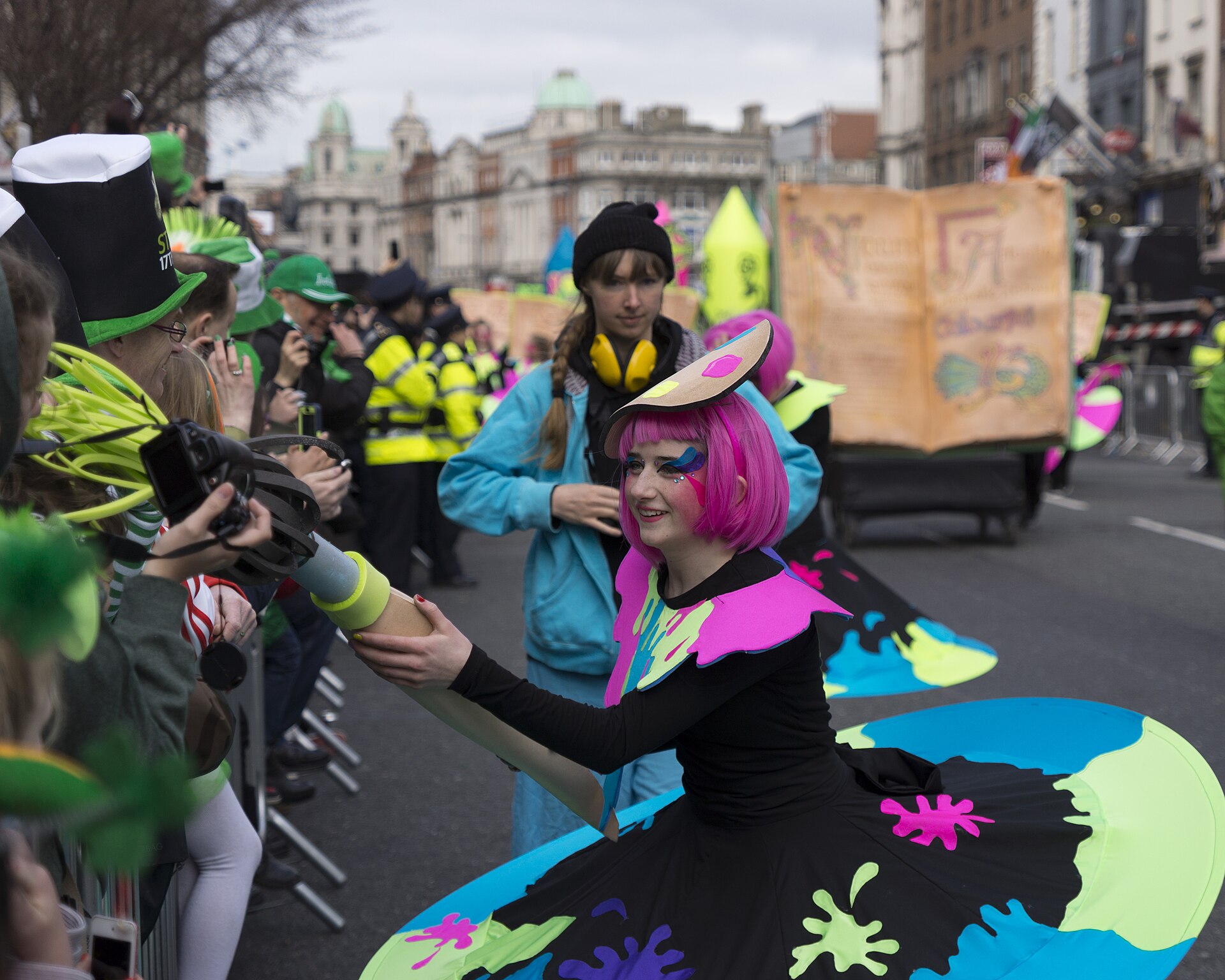 A pink-haired performer in a colourful skirt greets spectators behind barriers during Dublin's St Patrick's Day parade on Dame Street.