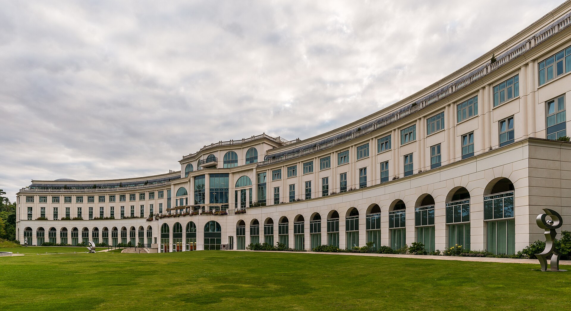 Powerscourt Hotel in County Wicklow curves around a green lawn, with arched windows and outdoor sculptures beneath cloudy skies.