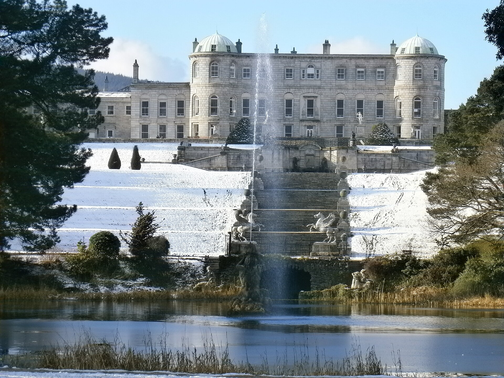 Powerscourt House overlooks snow-covered garden terraces and a fountain rising from the lake below.