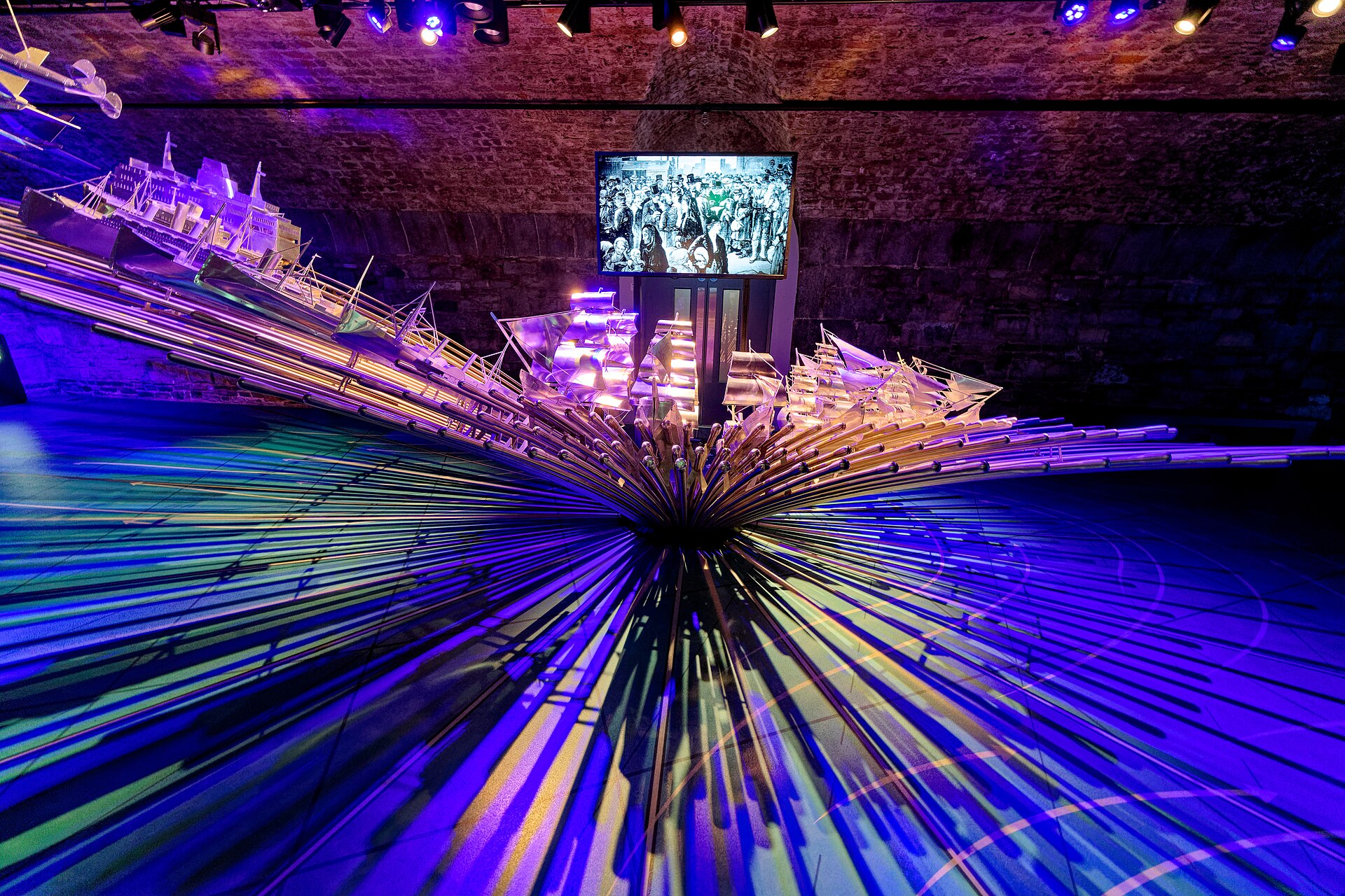 Purple lighting illuminates an installation of small model vessels and radiating rods beneath a stone vault at EPIC in Dublin.