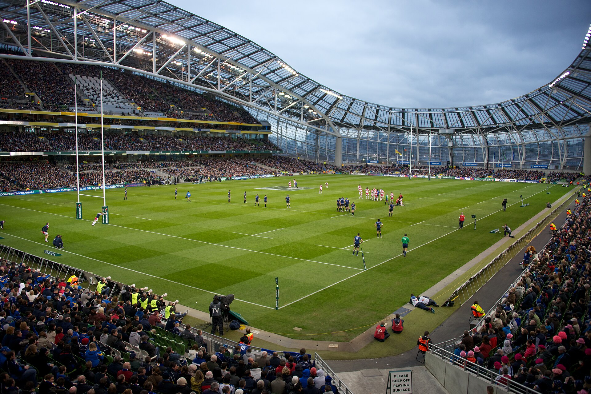 Rugby players line up on the Aviva Stadium pitch in Dublin beneath its curved roof and crowded spectator stands.