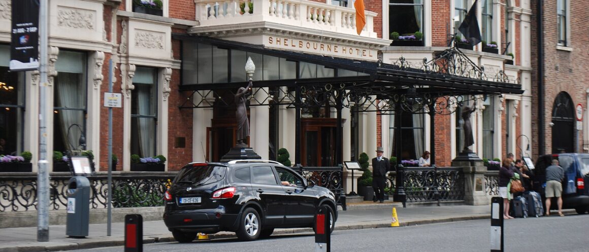 The Shelbourne Hotel entrance in Dublin, with flags above its canopy and people standing beside the ornate railings.