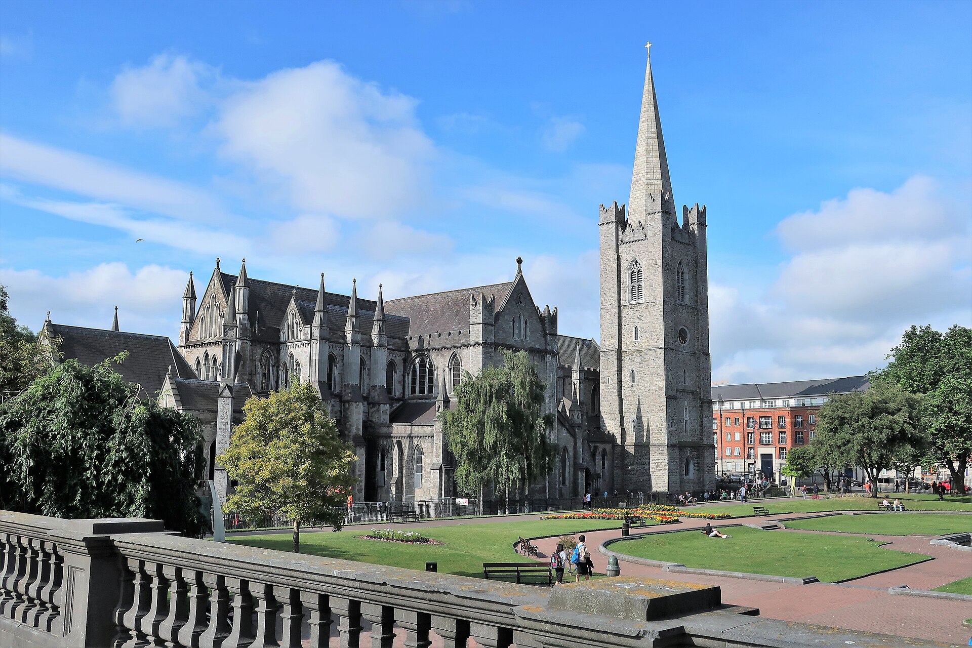 St Patrick's Cathedral in Dublin rises above park lawns, with its square tower and spire against blue sky.