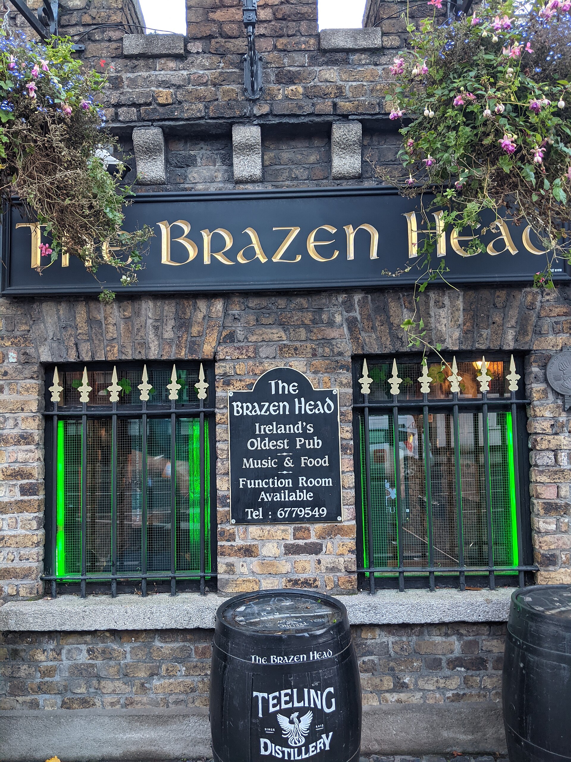 Stonework and green window frames beneath the Brazen Head sign in Dublin, with hanging plants and a barrel outside.