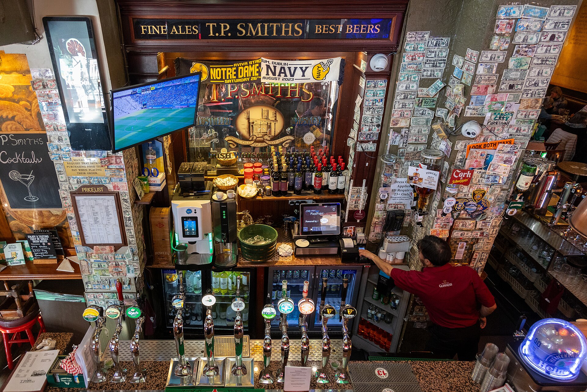 Taps face wooden shelves at T.P. Smith's in Dublin, with banknotes covering the pillars beside a bartender.