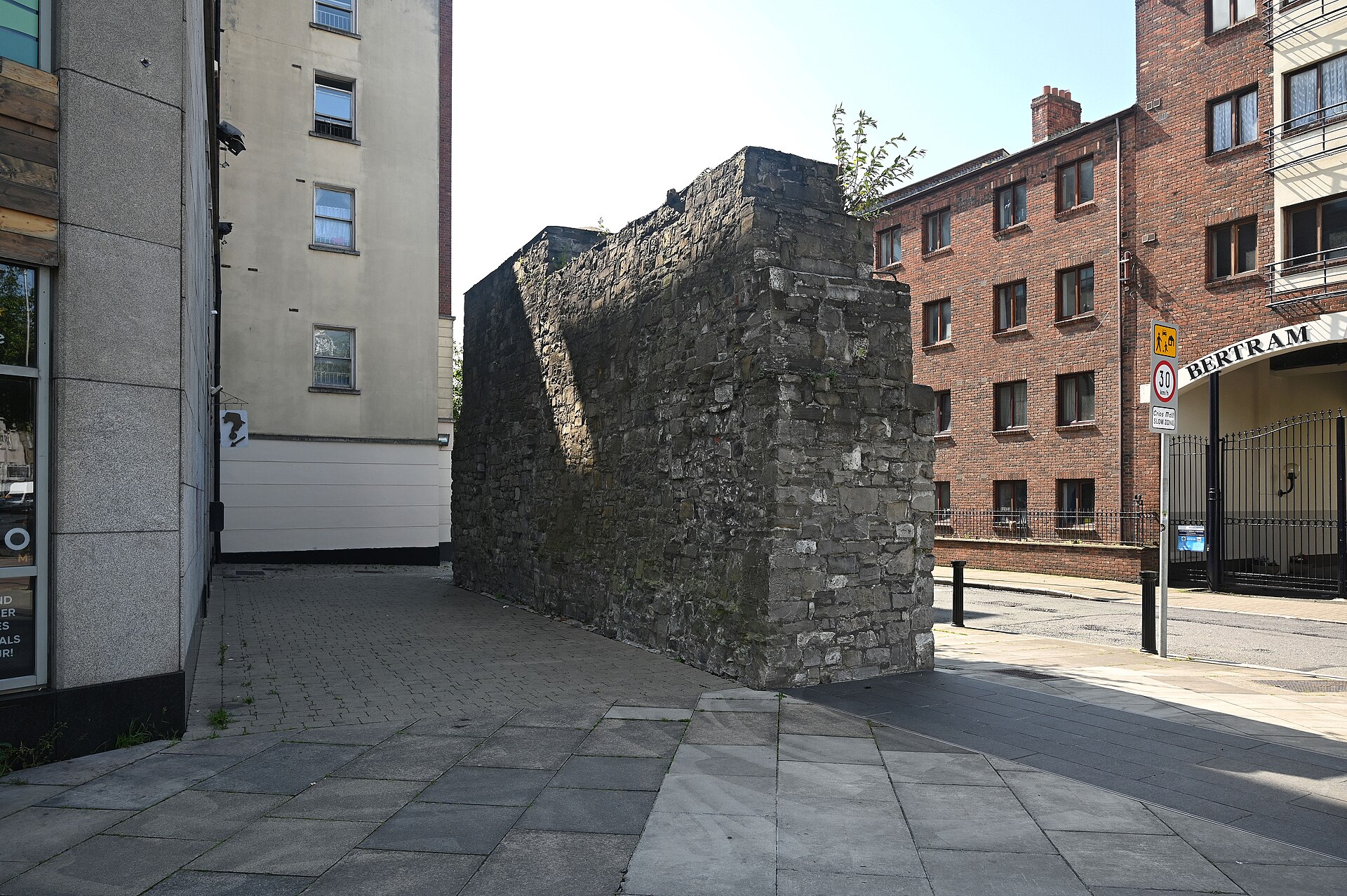 A thick section of Dublin's medieval city wall stands beside the pavement at Lamb Alley, surrounded by modern buildings.