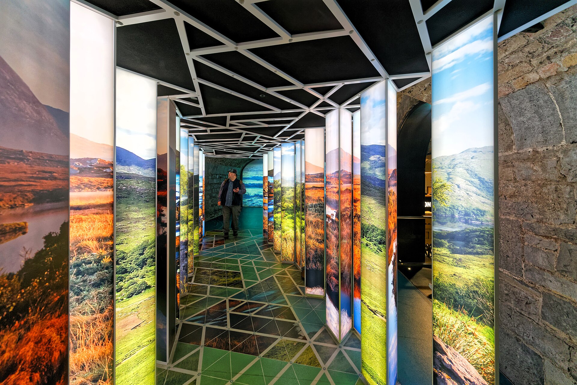 A visitor walks between illuminated landscape panels and stone walls inside EPIC The Irish Emigration Museum in Dublin.