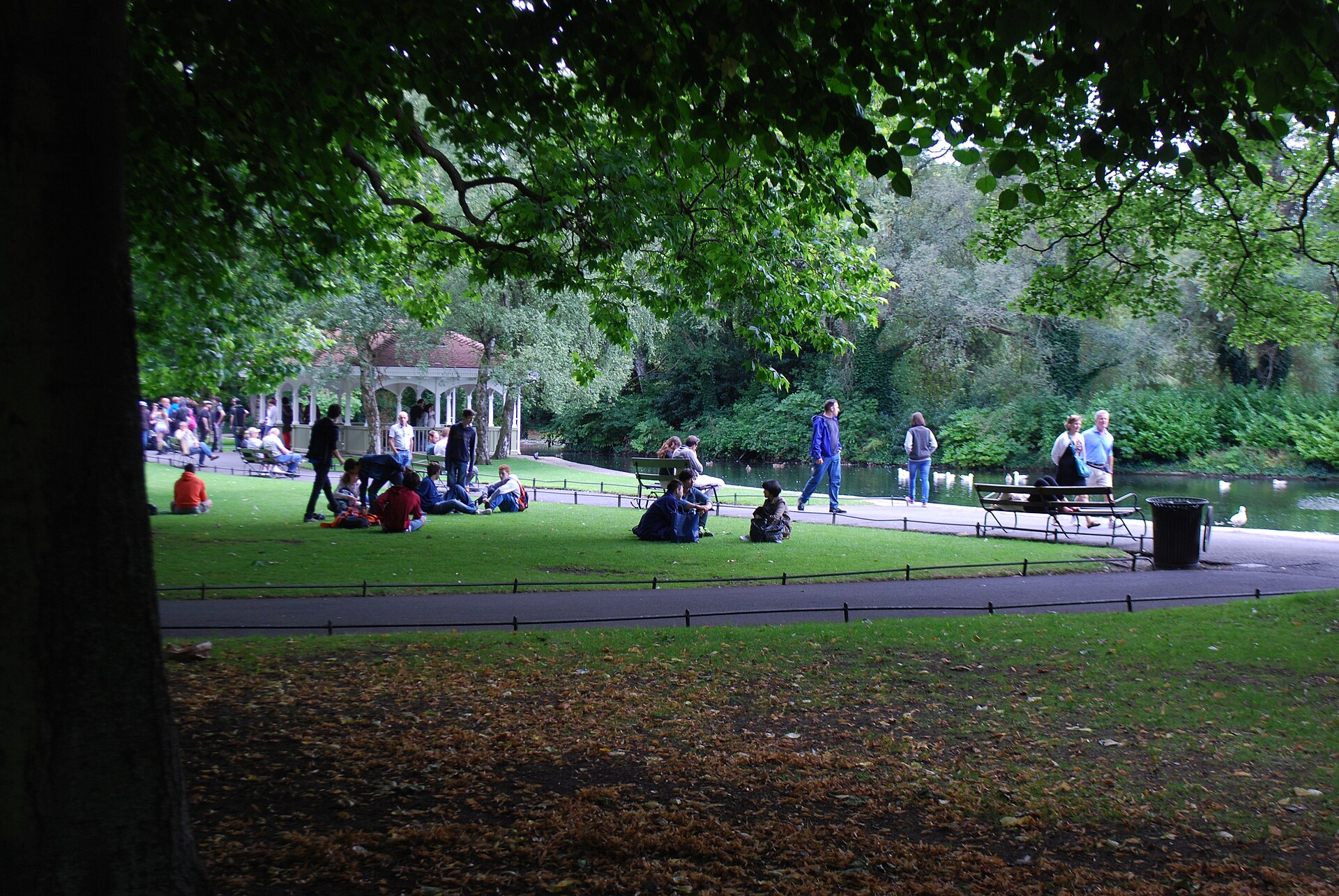 Visitors sit on shaded grass beside the pond and gazebo in St Stephen’s Green, Dublin.