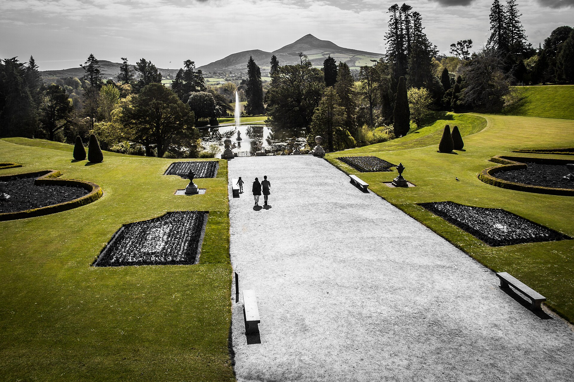 Visitors walk between formal lawns at Powerscourt, with a fountain and mountain rising beyond the terraced garden.