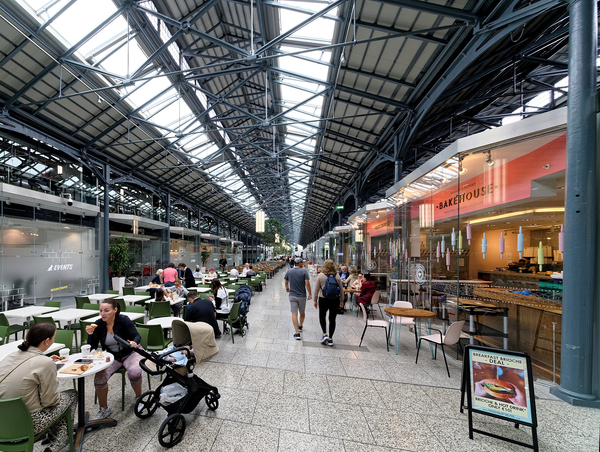 Visitors walk between tables and shops beneath the exposed iron roof and skylights inside Dublin's CHQ Building.