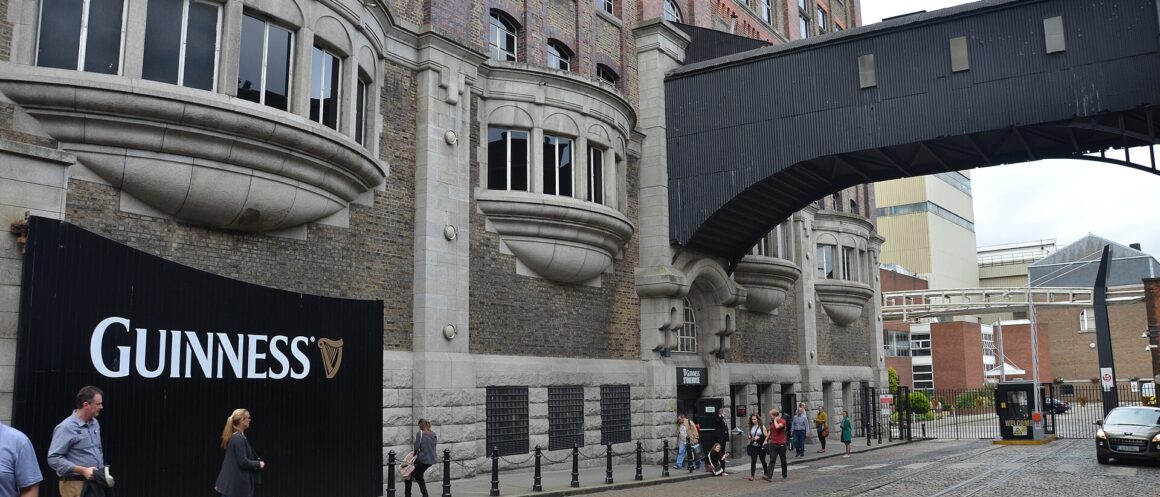 Visitors walk past the Guinness Storehouse’s brick and stone exterior beneath a covered bridge in Dublin.