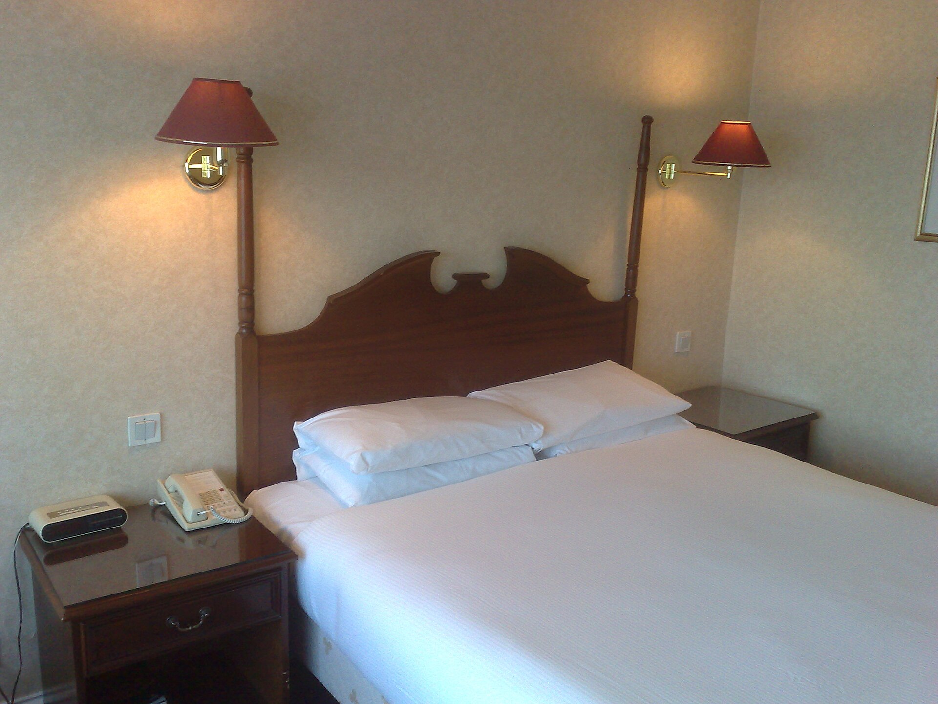 A white double bed with a wooden headboard, wall lamps and bedside tables in the Burlington Hotel in Dublin.