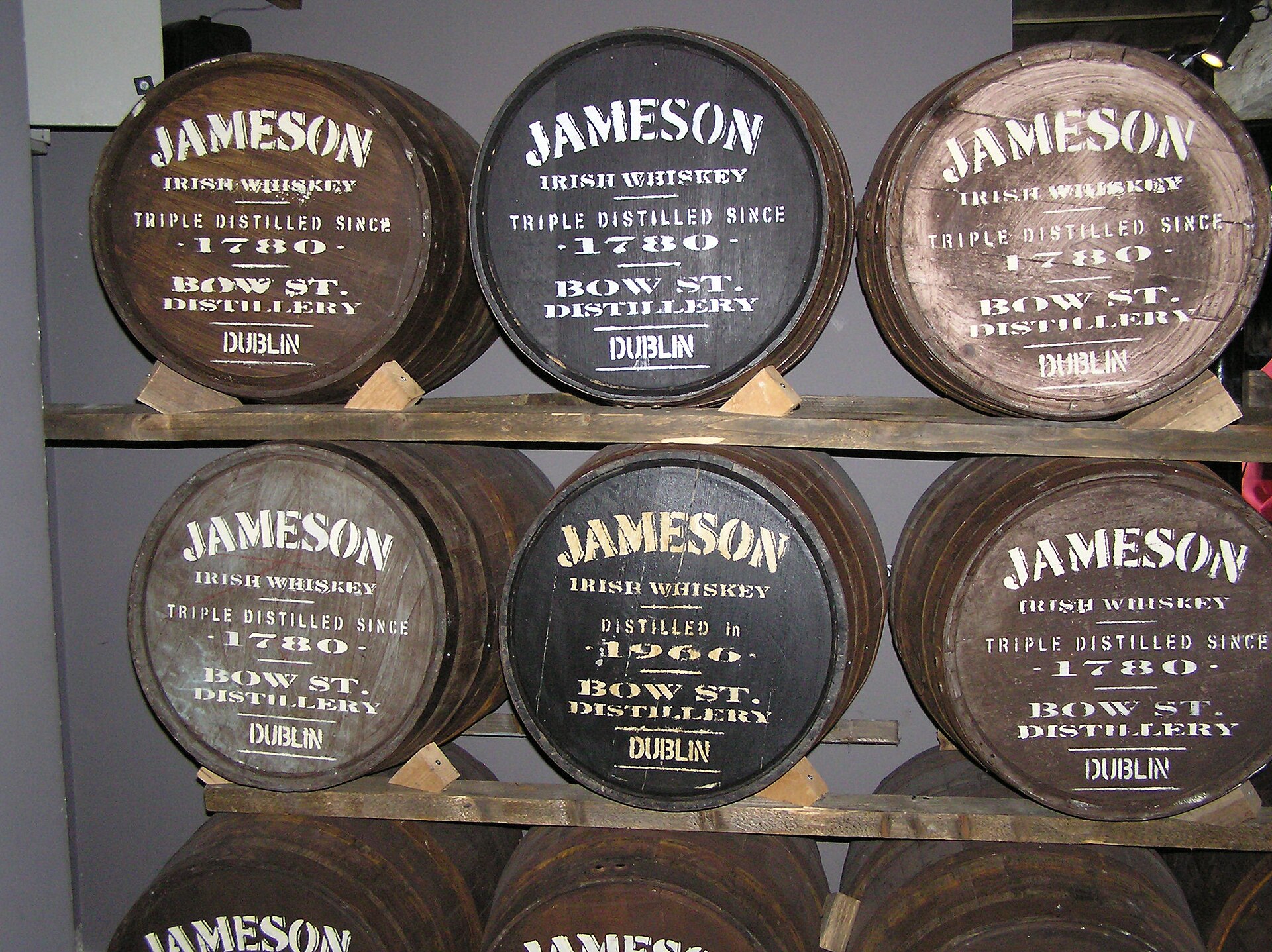 Wooden barrels are stacked on racks at Jameson Distillery in Dublin, with white Bow St lettering across their dark ends.