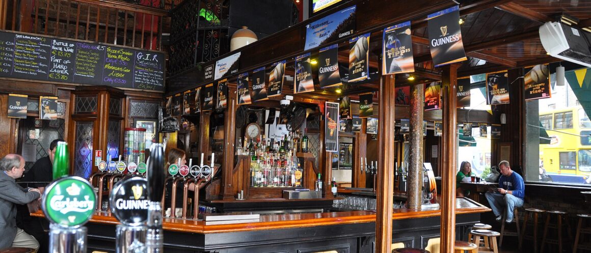 Wooden stools line the polished bar at the Bleeding Horse in Dublin, beneath a timber ceiling and mirrored shelves.