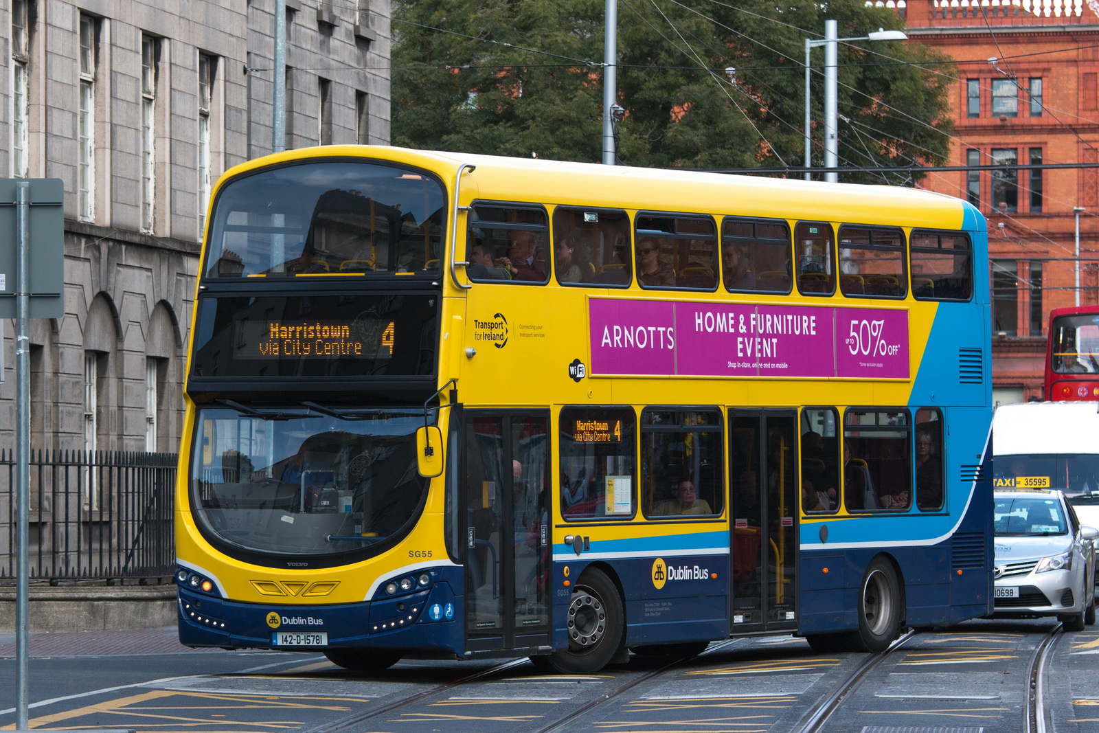 A yellow and blue Dublin Bus double-decker travels along a Dublin street with tram rails and stone buildings.